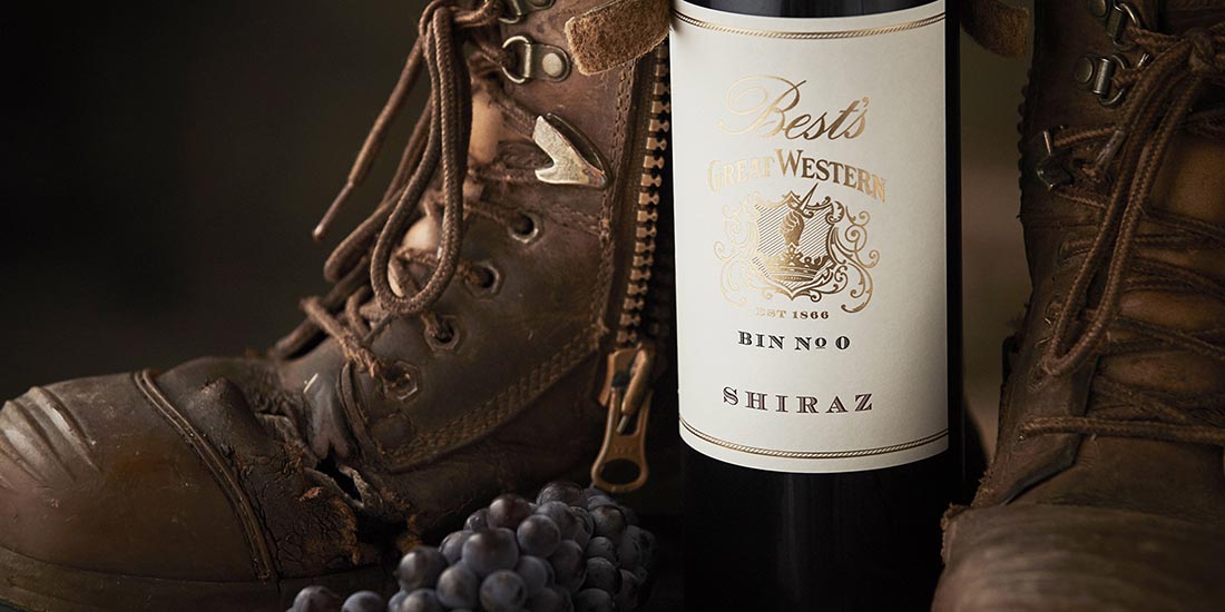 A bottle of shiraz beside a boot and grapes.